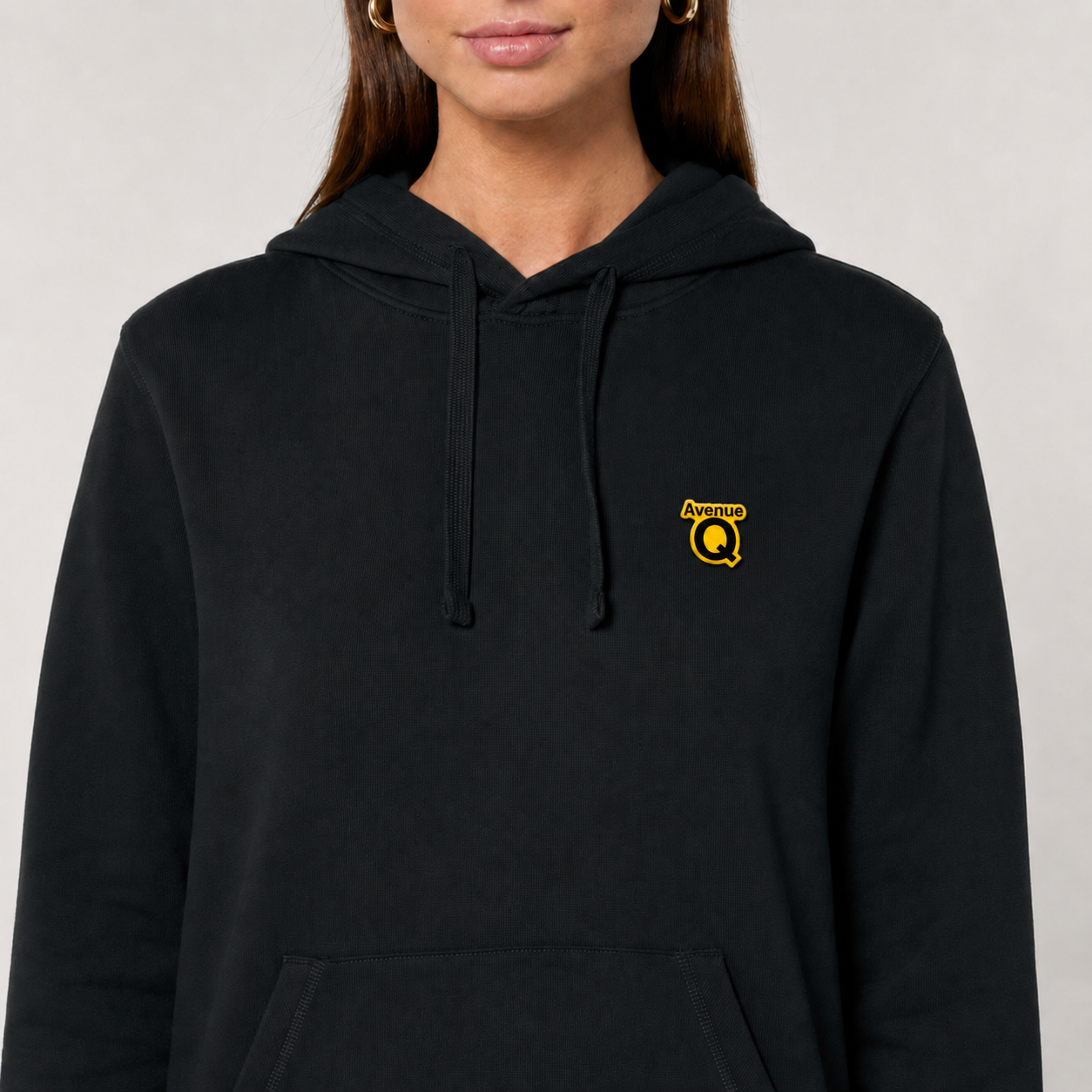 Official Avenue Q pin badge worn on a black hoodie at chest level