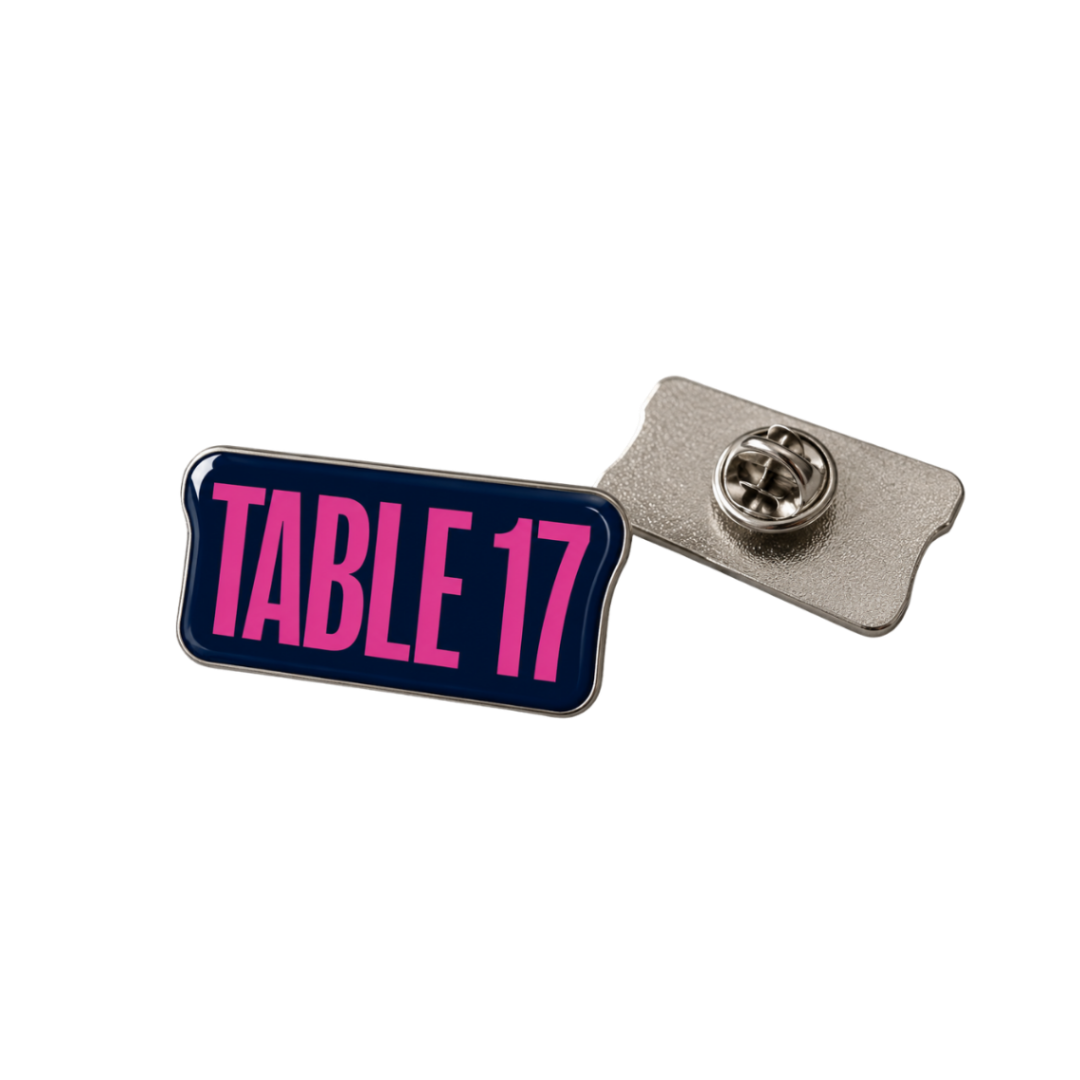 A rectangular enamel pin with rounded corners featuring the text 'TABLE 17' in bright pink on a dark navy background, shown with its silver metal clutch backing on a plain white background.